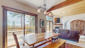 Un comedor amplio con una mesa y bancos de madera, ventanas grandes con vistas y una zona de estar acogedora con un sofá de cuero.