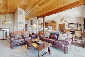 A spacious living area with leather sofas, a wooden coffee table, and a kitchen in the background. - Mountain home with  fireplace, partial lake views from deck & hot tub (Tahoe City)