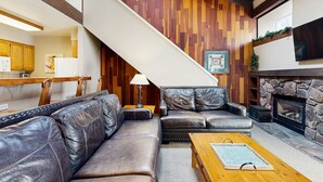 Een woonkamer met een open haard, leren banken, een houten salontafel en een trap.