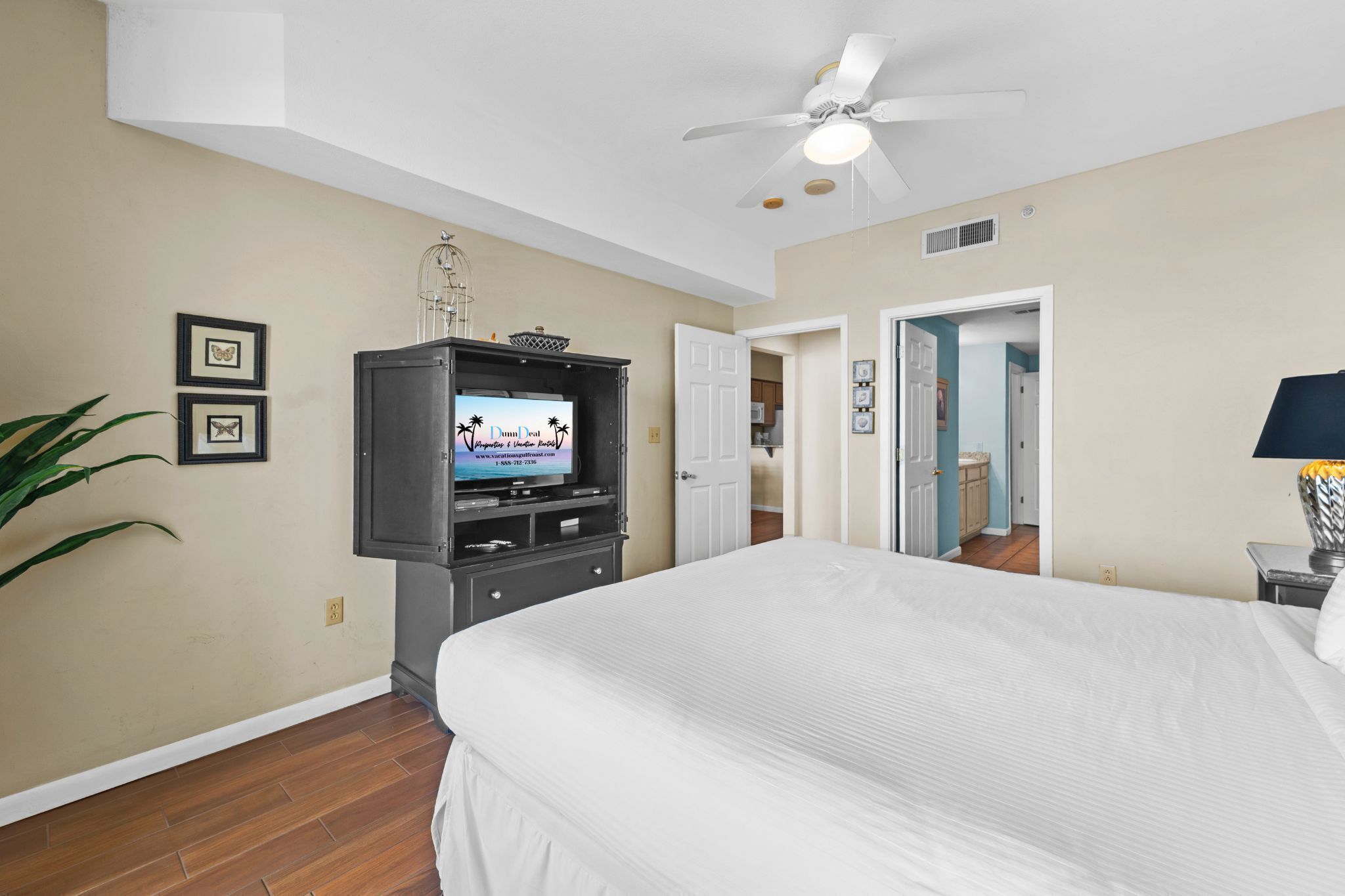 A hotel room with a bed, a television, a ceiling fan, and a door leading to a bathroom.