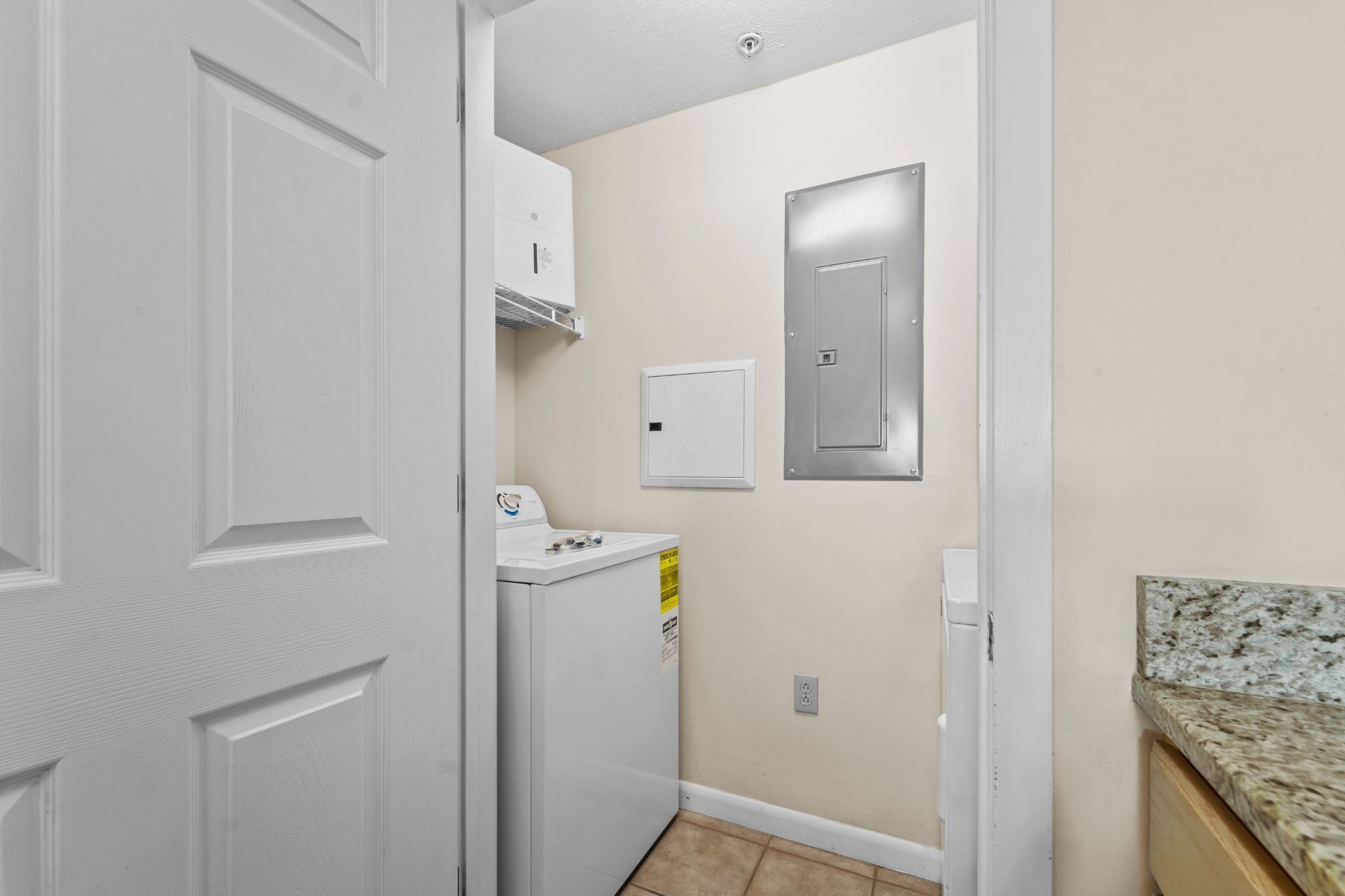 Een wasruimte met een wasmachine en droger, een thermostaat, en een deur naar een andere kamer.