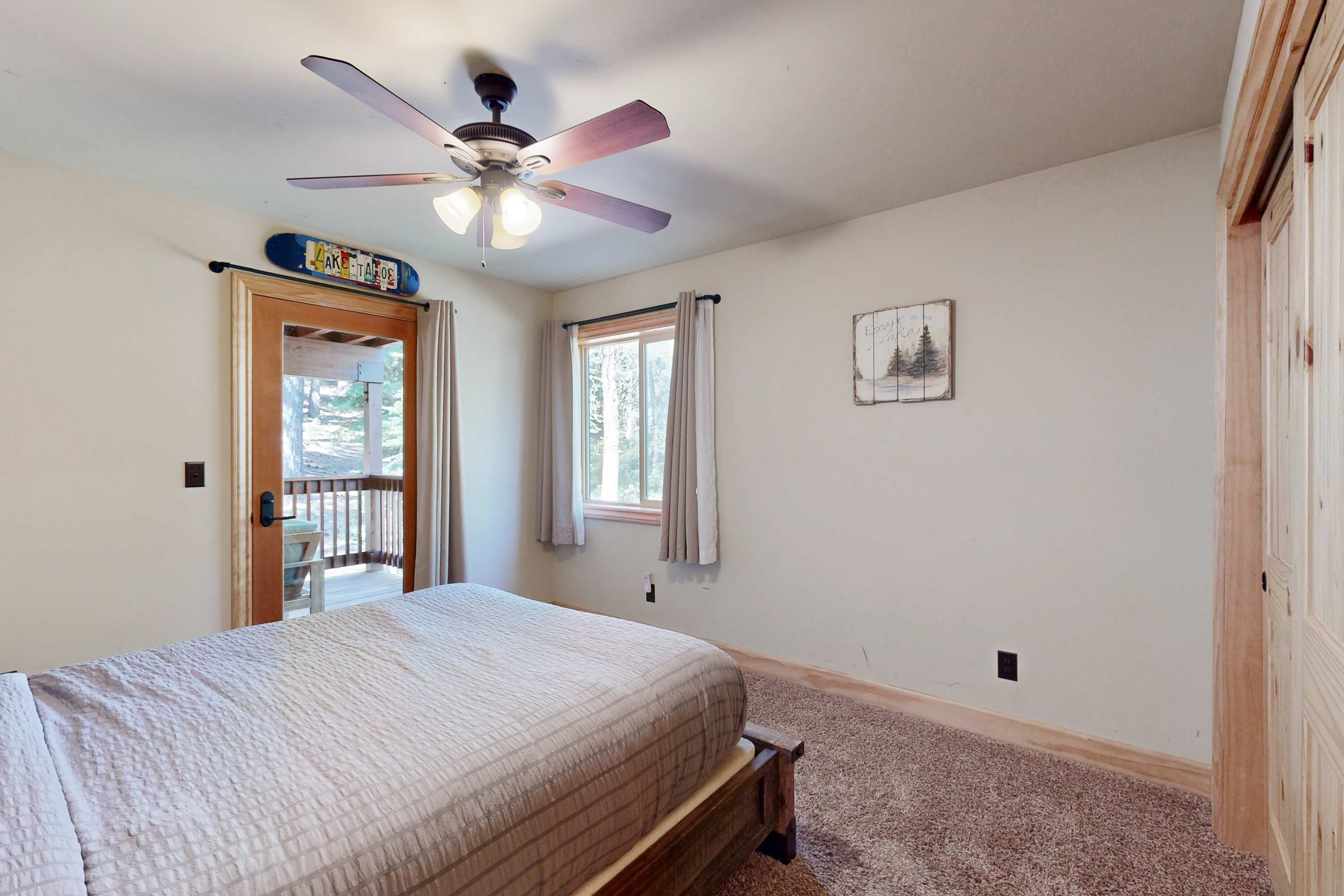 A bedroom with a bed, a ceiling fan, a window with curtains, a door leading to a balcony, and a small picture on the wall.