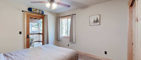 A bedroom with a bed, a ceiling fan, a window with curtains, a door leading to a balcony, and a small picture on the wall.