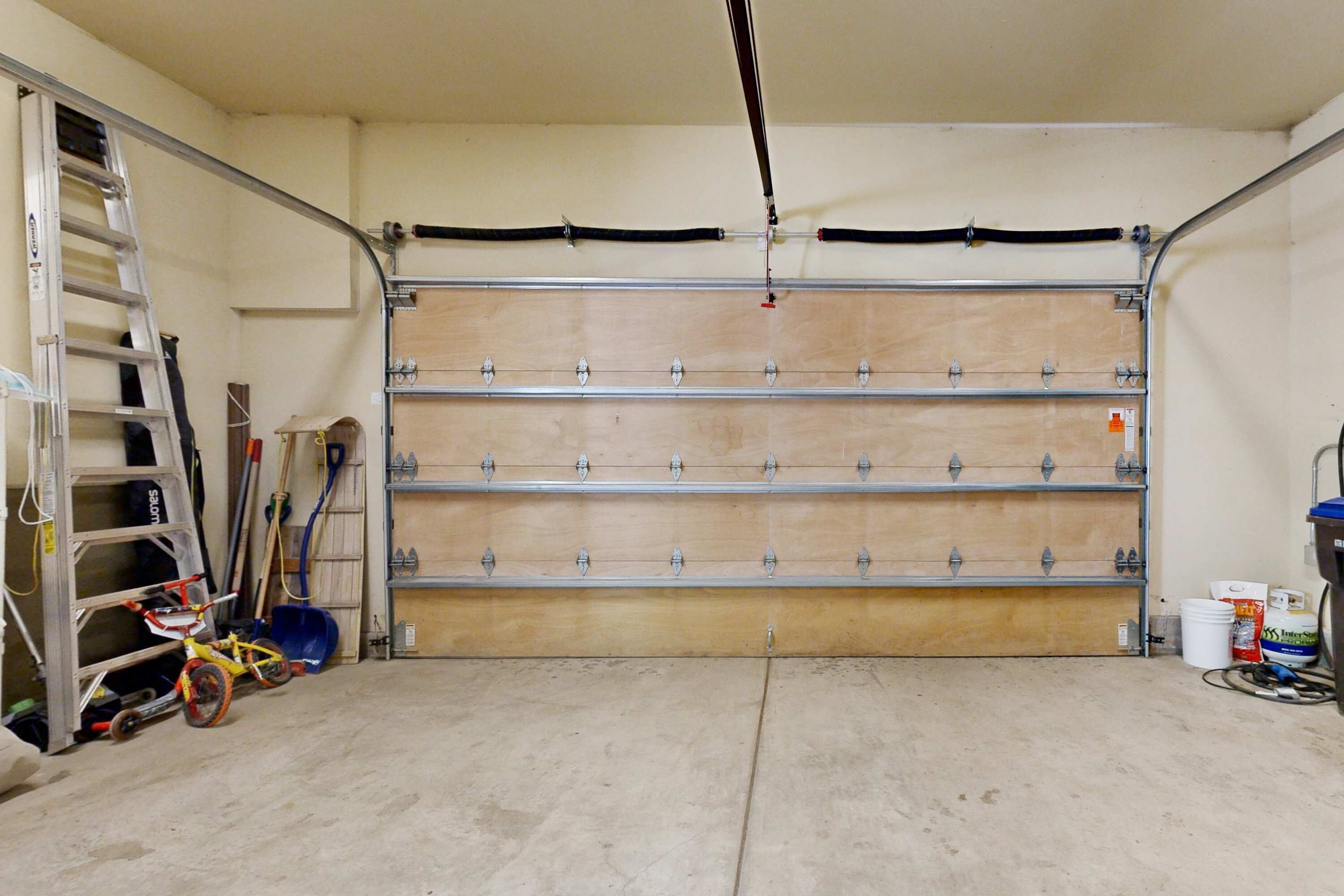 A garage with a wooden door, a ladder, a bicycle, and cleaning supplies.