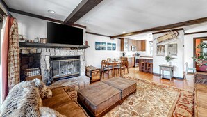 A living room with a stone fireplace, a television, and a large fur rug. - Ski getaway with amazing mountain views, fireplace, pool, & river path access (Olympic Valley)