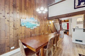 Ein Essbereich mit Holzwandverkleidung, einem langen Tisch, Stühlen, einer Kristallleuchtre und einer Treppe, die zu einer oberen Ebene führt.