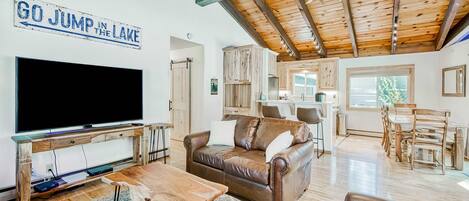 A spacious living room with a large flat-screen TV, a brown leather sofa, a wooden coffee table, and a ceiling fan.