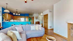 A living room with a sofa, pillows, a ceiling fan, pendant lights, and a kitchen in the background. - Centrally-Located Condo near Ski Resorts with Gas Fireplace (Truckee)