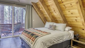 A bedroom with a large bed, a wooden ceiling, and a sliding glass door leading to an outdoor area with a chair and table. - All-season, dog-friendly cabin with fireplace & deck - near Heavenly & beach (South Lake Tahoe)
