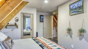 A bedroom with a bed, a wooden ceiling, a door, a mirror, a wall-mounted shelf, and a framed picture. - All-season, dog-friendly cabin with fireplace & deck - near Heavenly & beach (South Lake Tahoe)