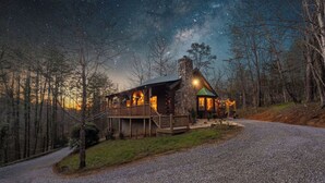Eine Blockhütte mit Veranda, umgeben von einem Schotterweg und einem Wald.