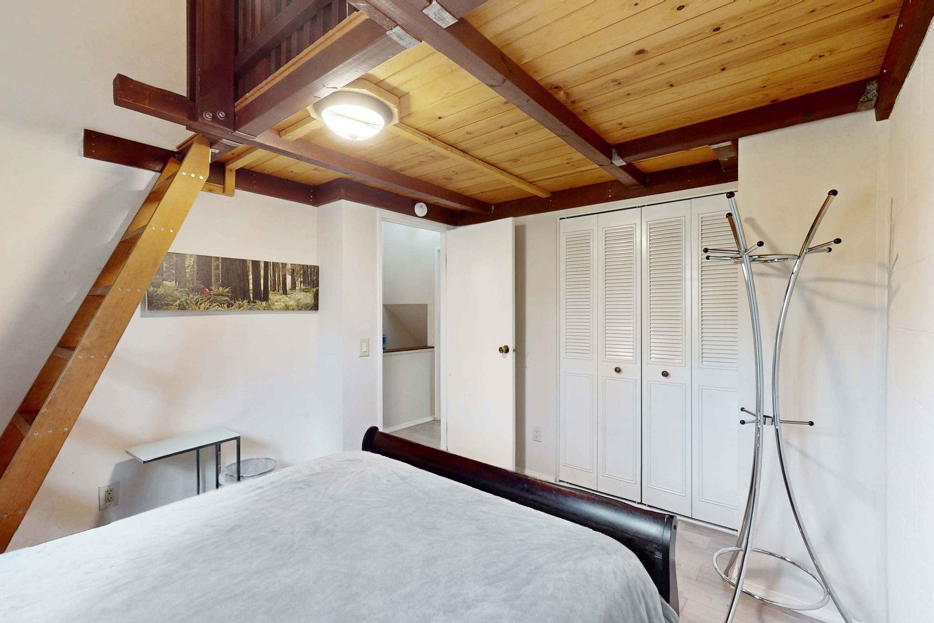 A bedroom with a sloped ceiling, a bed, a wardrobe, and a coat rack.