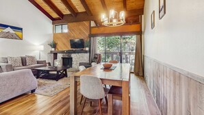 Un salón amplio con techo de madera, chimenea, una mesa de comedor con sillas, un sofá y televisión.