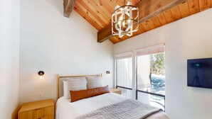 Une chambre à coucher avec un lit, une table de chevet en bois, un téléviseur fixé au mur et une fenêtre donnant sur un beau paysage.