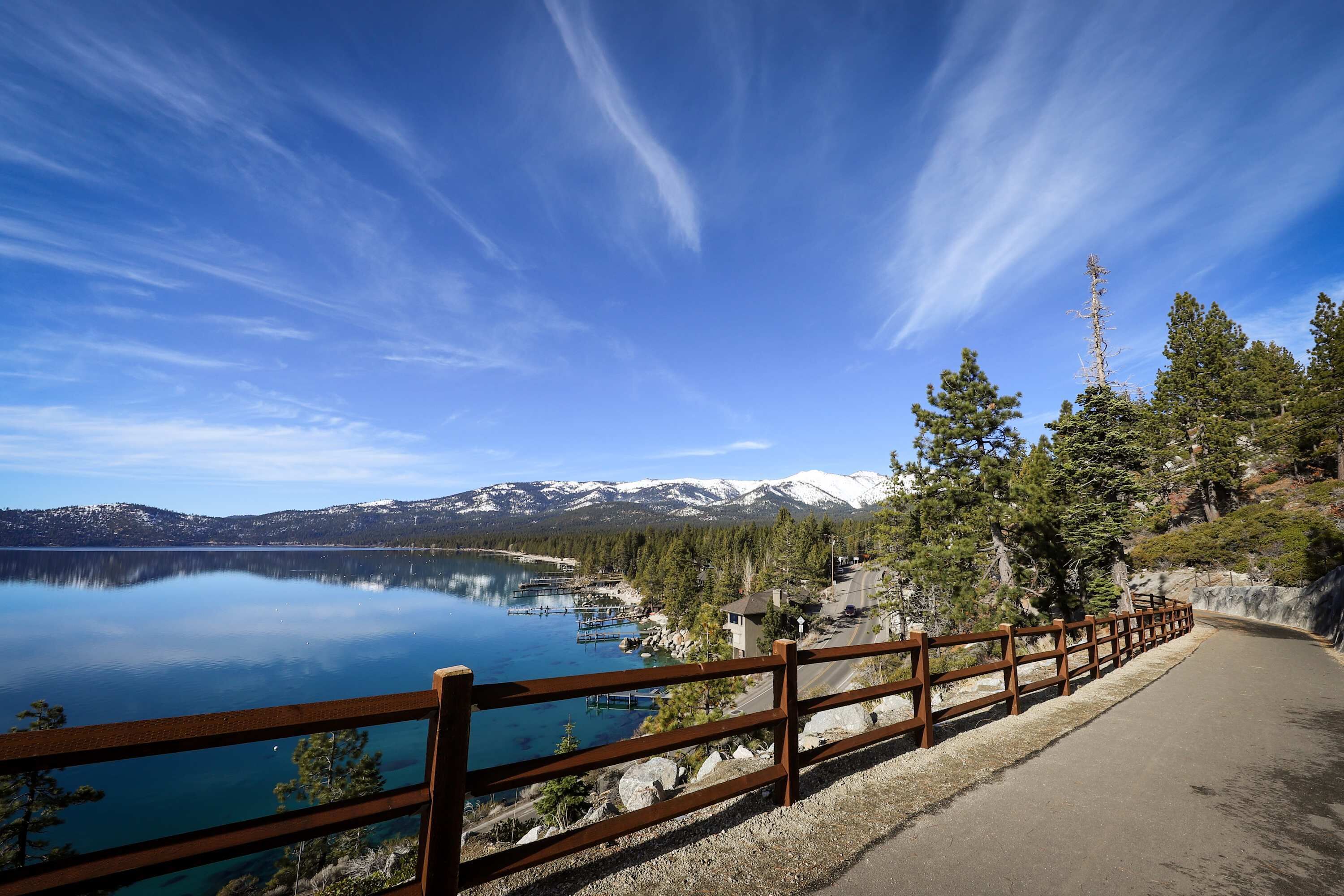 Une vue pittoresque d’un lac, avec une clôture en bois, un ciel dégagé et des montagnes enneigées en arrière-plan.
