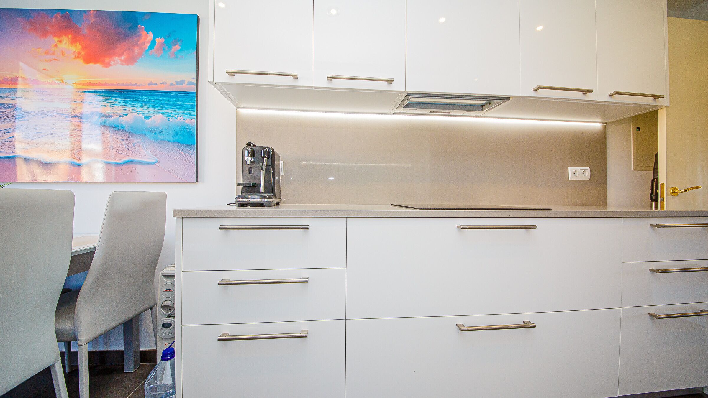 Een moderne keuken met witte kastjes, een ingebouwde koffiezetapparaat en uitzicht op de oceaan door een groot raam.