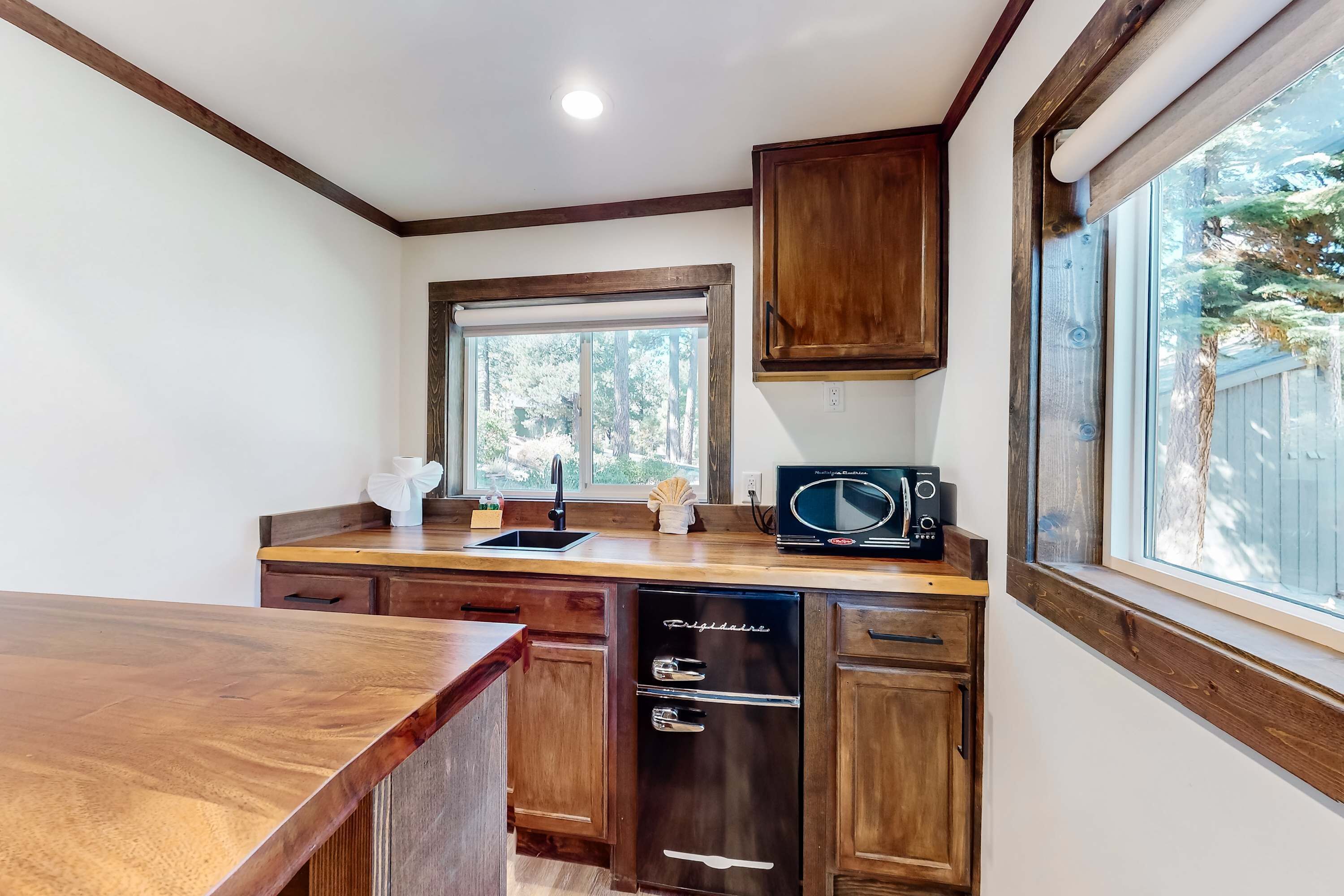 Cocina con armarios de madera, lavavajillas, microondas y ventana con vista a árboles.