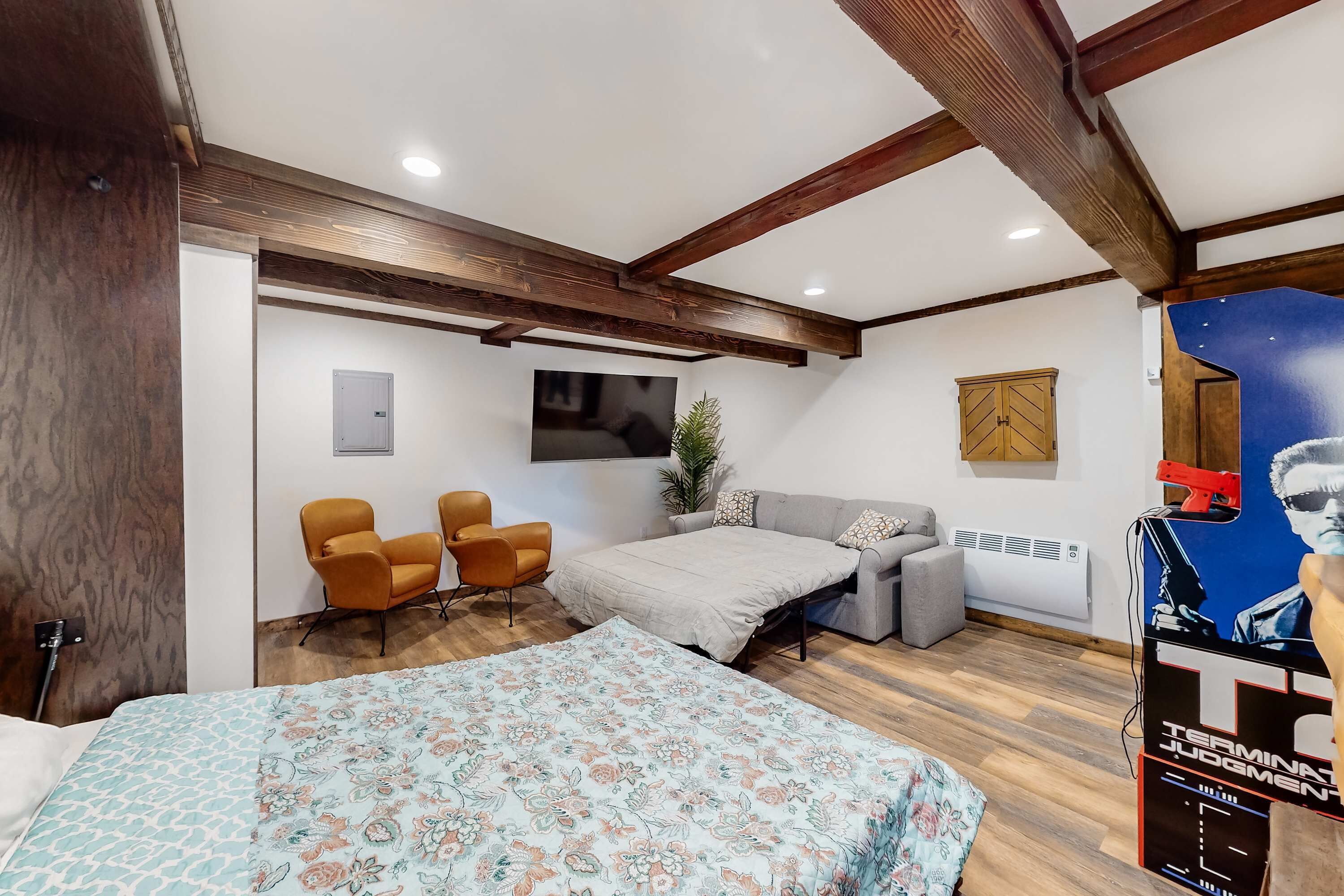 A room with a bed, two chairs, a sofa, a TV, and a poster.