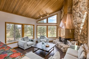 A spacious living area with large windows, a stone fireplace, and modern furniture. - Home with amazing views, outdoor dining, fireplaces, pool- dogs ok (Truckee)