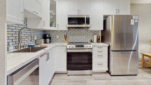 Una cocina moderna con armarios blancos, un refrigerador de acero inoxidable, un microondas, un horno y un lavamanos con grifo.