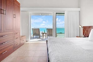 A bedroom with a large bed, a wooden wardrobe, and a balcony with chairs and a table. - Private Beach,  Amazing Views, Stunning Amenities! (Turks and Caicos Islands)