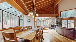 A spacious dining area with a wooden table and chairs, large windows, and a stone fireplace. - Inviting home in Northstar Ski Resort with private hot tub & sauna, pool access (Truckee)