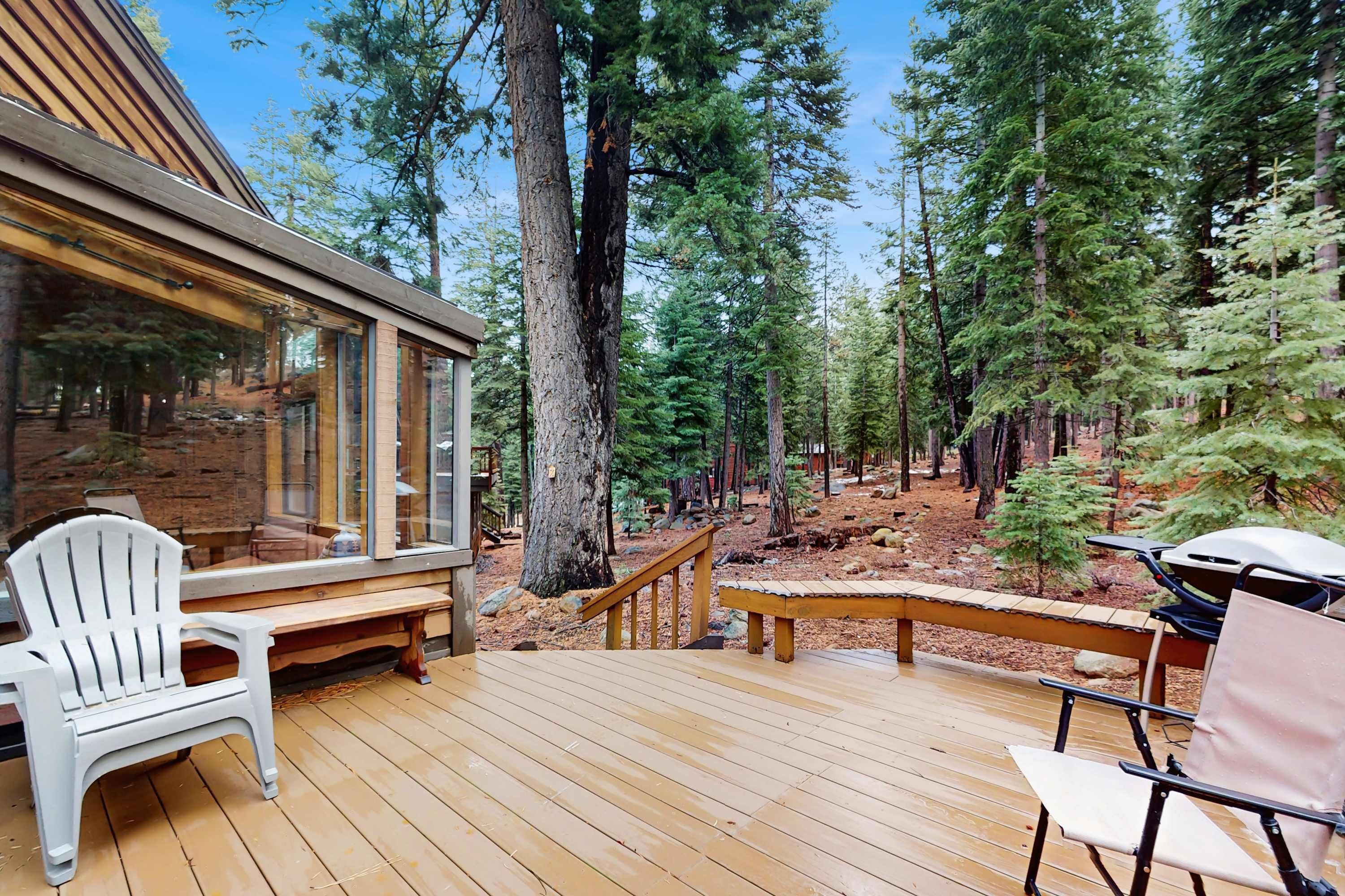 Une terrasse en bois avec un fauteuil Adirondack blanc, un banc et un espace barbecue.