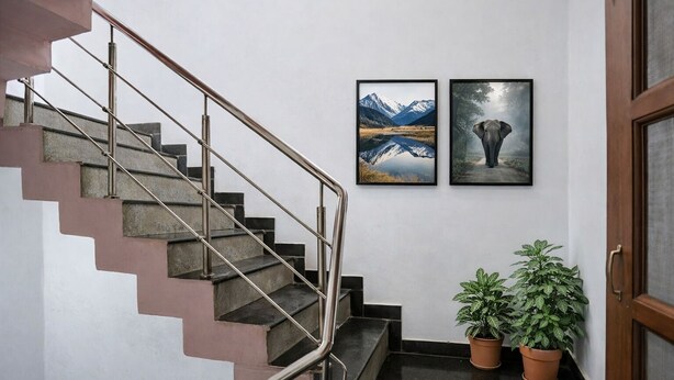 Un escalier avec des rampes en métal, deux tableaux encadrés accrochés au mur et deux plantes en pot.