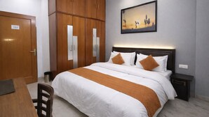Une chambre d’hôtel avec un lit, un bureau, une armoire et un tableau au mur.