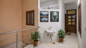 Un escalier avec une rampe en métal, un évier blanc, deux plantes en pot et des tableaux encadrés au mur.
