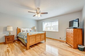 Ein Schlafzimmer mit einem hölzernen Bett, einem Deckenventilator, einem Schminktisch, einem Fernseher und einem Fenster.