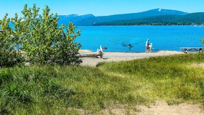 Uitzicht op een meer met een picknicktafel en een bankje, omringd door groen en bergen op de achtergrond.