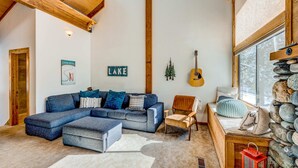 Un salón acogedor con un sofá modular, una silla de madera, una guitarra y una pared de piedra.