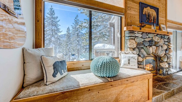 Un rincón acogedor con una chimenea de piedra, un ventanal con vistas nevadas y un cojín con motivos de oso.