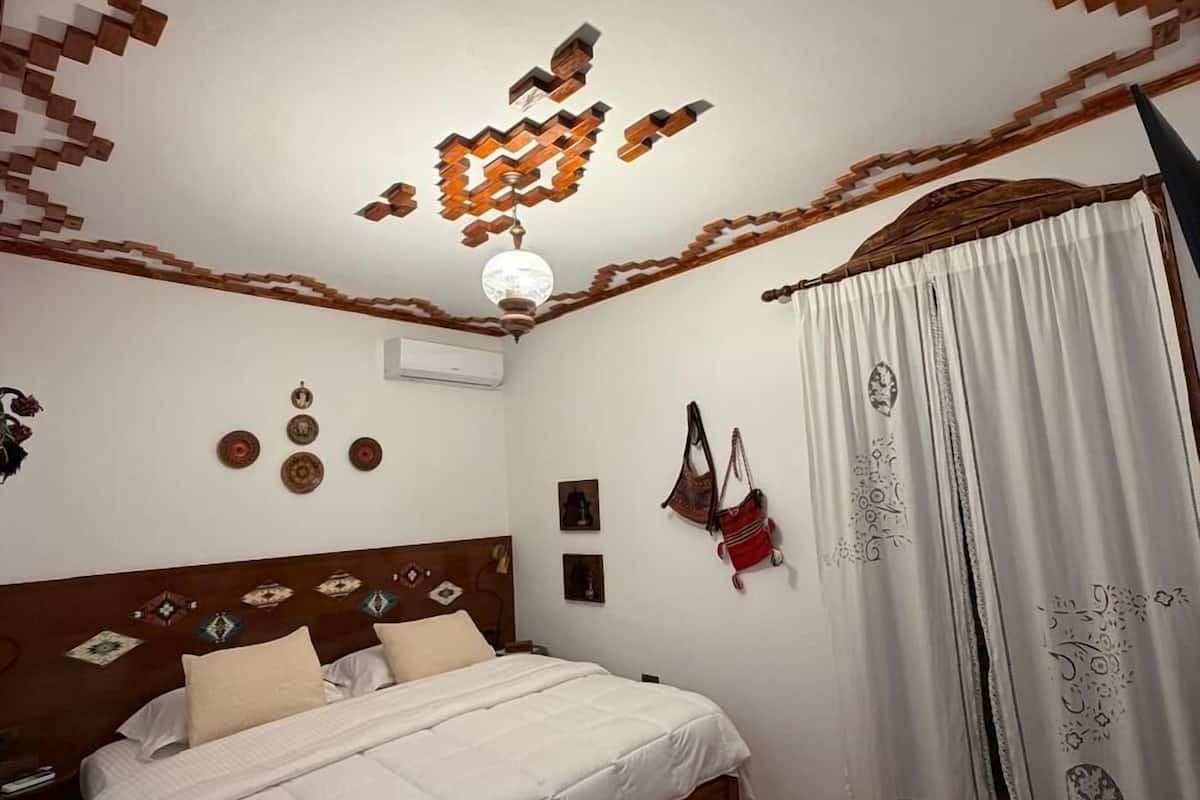Ein Schlafzimmer mit einem Bett, einem gemusterten Teppich, einer Deckenleuchte und einem Fenster mit Vorhängen.