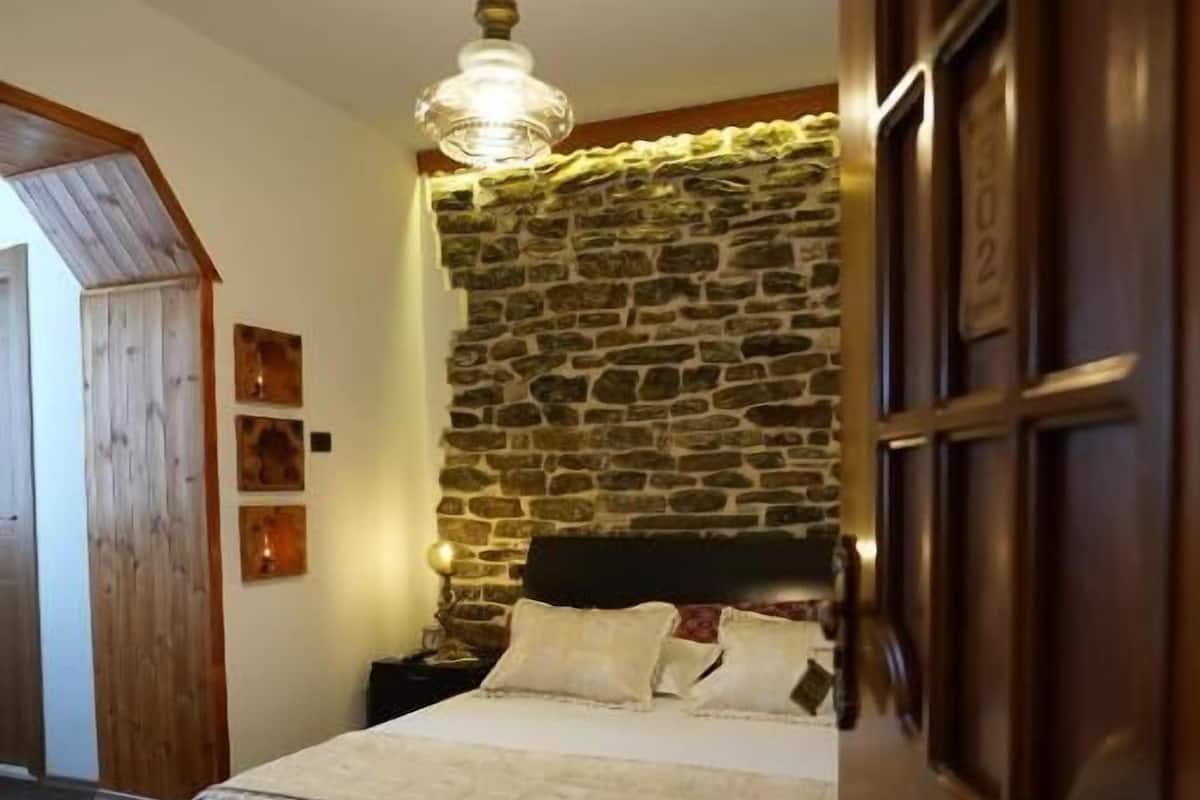 Ein Schlafzimmer mit Steinsandsteinwand, einem Bett mit Kopfteil, einer Holztür und einer Deckenleuchte.