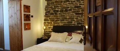 Un dormitorio con pared de piedra, cama con cabecera, puerta de madera y lámpara en el techo.