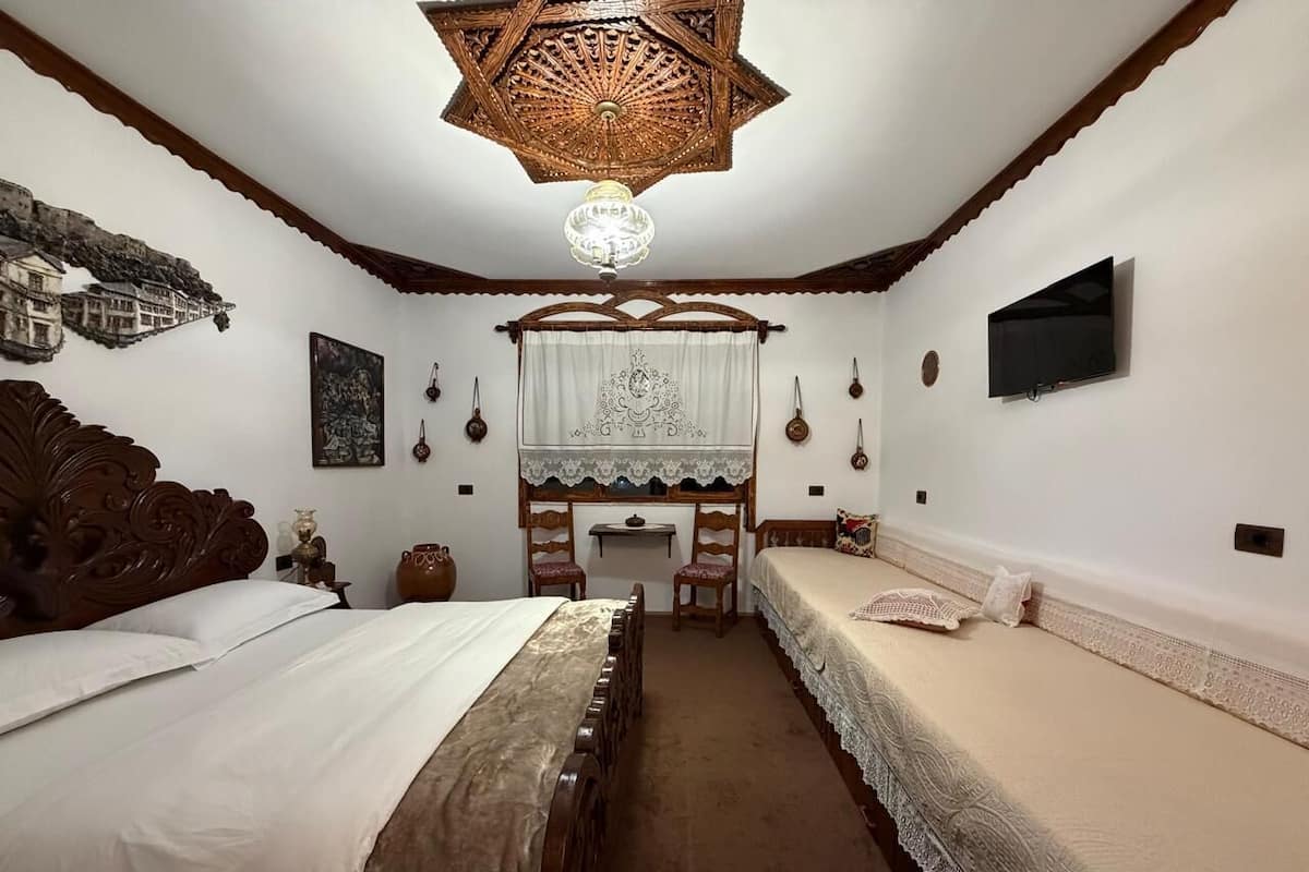 Ein traditionell eingerichteter Raum mit einem großen Bett, einem kleineren Bett, einem Kamin und einem an der Wand befestigten Fernseher.