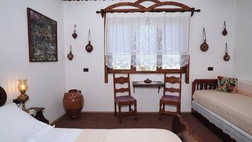 Una habitación tradicional con cama, dos sillones, una mesa, ventana con cortinas y lámparas fijadas a la pared.