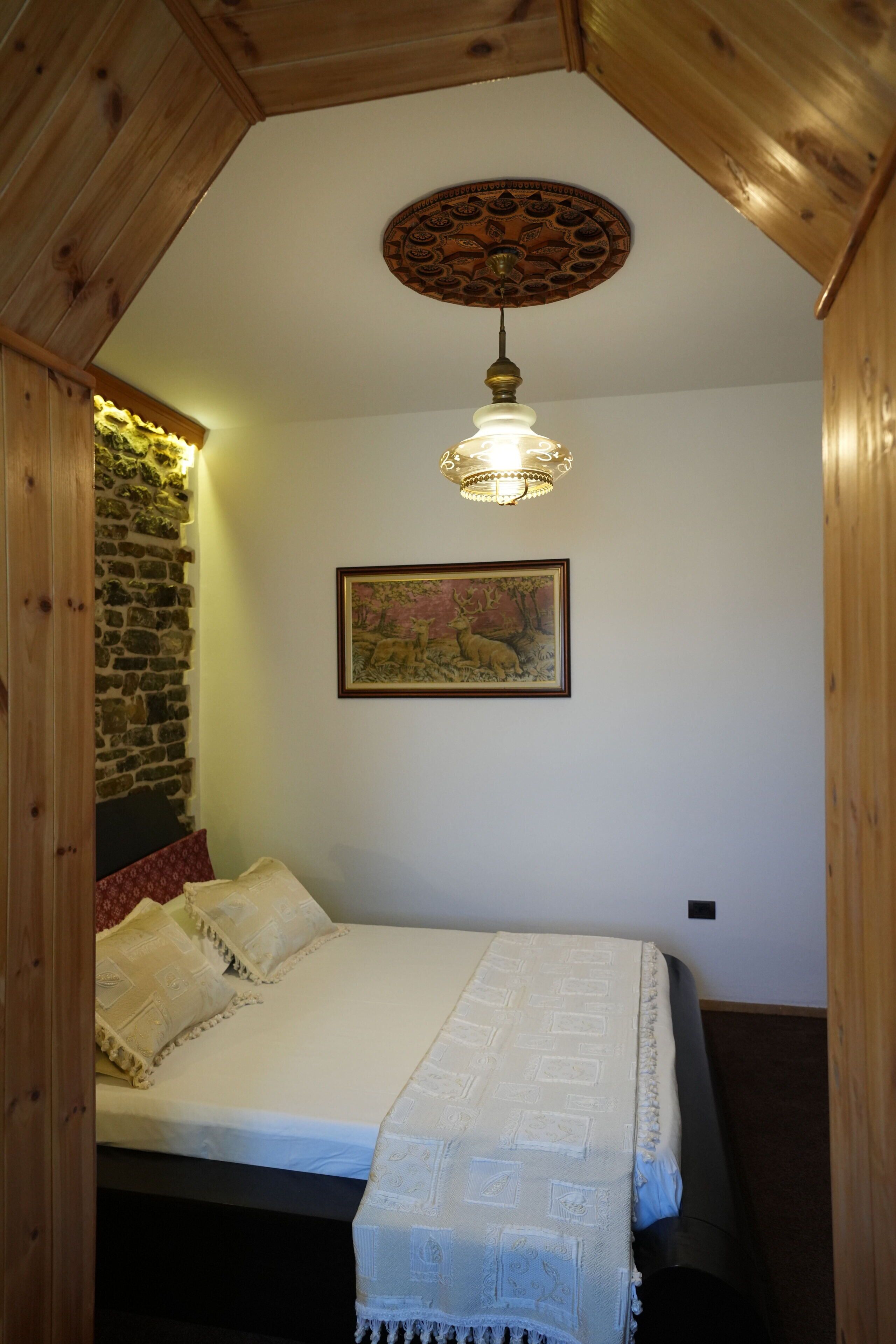 Un dormitorio con una cama, techo de madera, pared de piedra, un cuadro y una lámpara colgante.