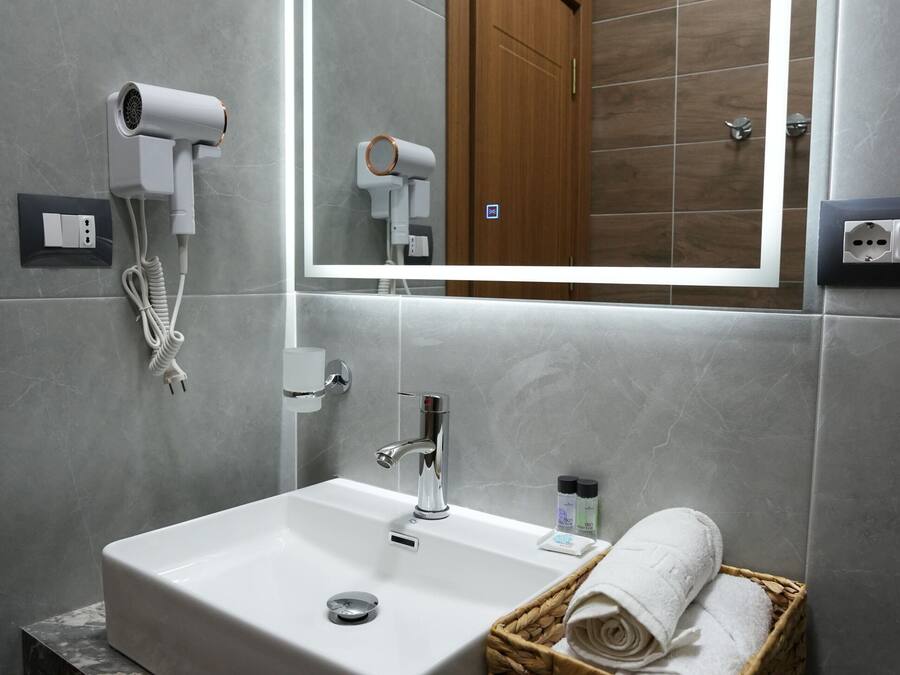 A bathroom with a white sink, a mirror, a hairdryer, a towel basket, and a wooden door.