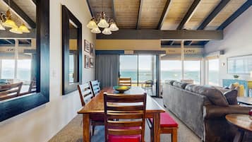 Un coin repas avec une table et des chaises en bois, un canapé et une vue sur l’océan.