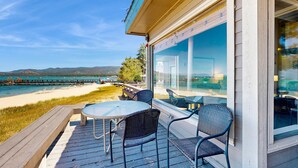 En træterrasse med et bord og stole med udsigt over en strand og en havn.