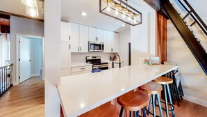 Une cuisine moderne avec des meubles blancs, un grand îlot central, des tabourets de bar et un escalier.