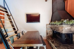 Un comedor con una mesa de madera, sillas, un televisor montado en la pared y una chimenea de piedra.