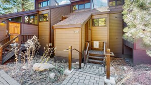 En modern byggnad i stugstil med en träfasad, en synlig garagedörr och en liten utomhustrappa som leder till entrén.