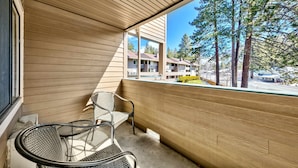 Ein Balkon mit Holzlatten, zwei Korbstühle und Blick auf ein Wohngebiet mit Bäumen und einem gelben Fahrzeug.