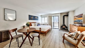 Ein modernes Hotelzimmer mit Bett, Kamin, Esstisch mit Stühlen, Sofa und großem Fenster.