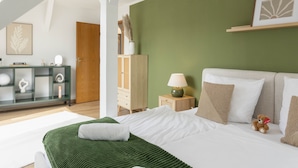 Une chambre à coucher avec un lit, une table de chevet, une lampe, un ours en peluche, une commode et un miroir.