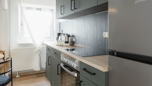Une cuisine moderne avec des meubles gris, un réfrigérateur en acier inoxydable, un plan de travail en bois et une fenêtre agrémentée de rideaux blancs.
